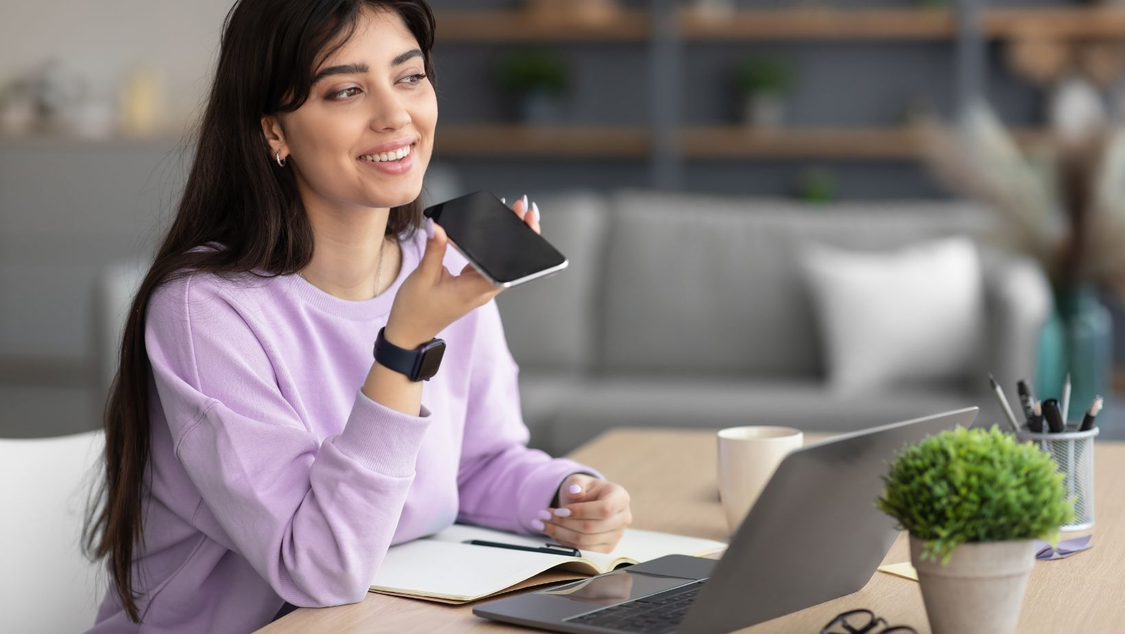 A business owner talking on her phone while at her desk on which there is a laptop and notebook