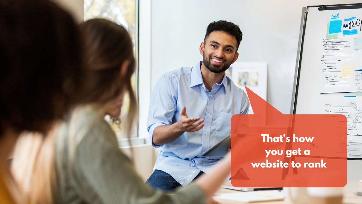 A man explains digital marketing terms to other people in a meeting room.